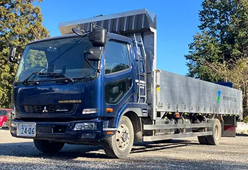 青いごみ収集車。企業名が車体に記載され、後部には圧縮機構が搭載されている。