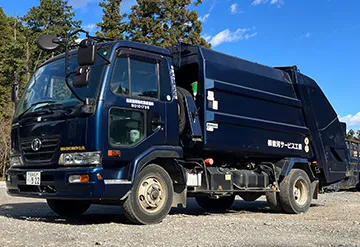 青いコンテナ運搬車。赤いリフト装置が搭載され、大型コンテナが積載されている。